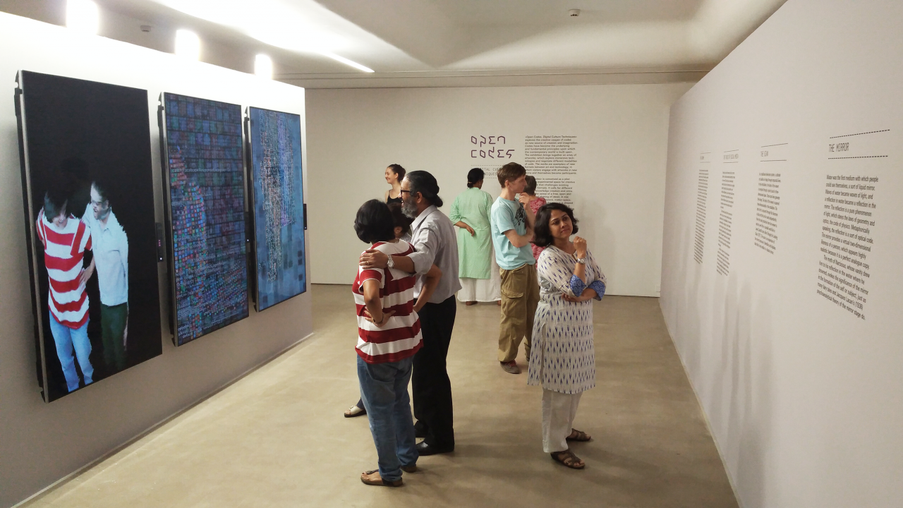 A group of people is standing in an exhibition space with white walls, reading the exhibition's texts or interacting with an installation.
