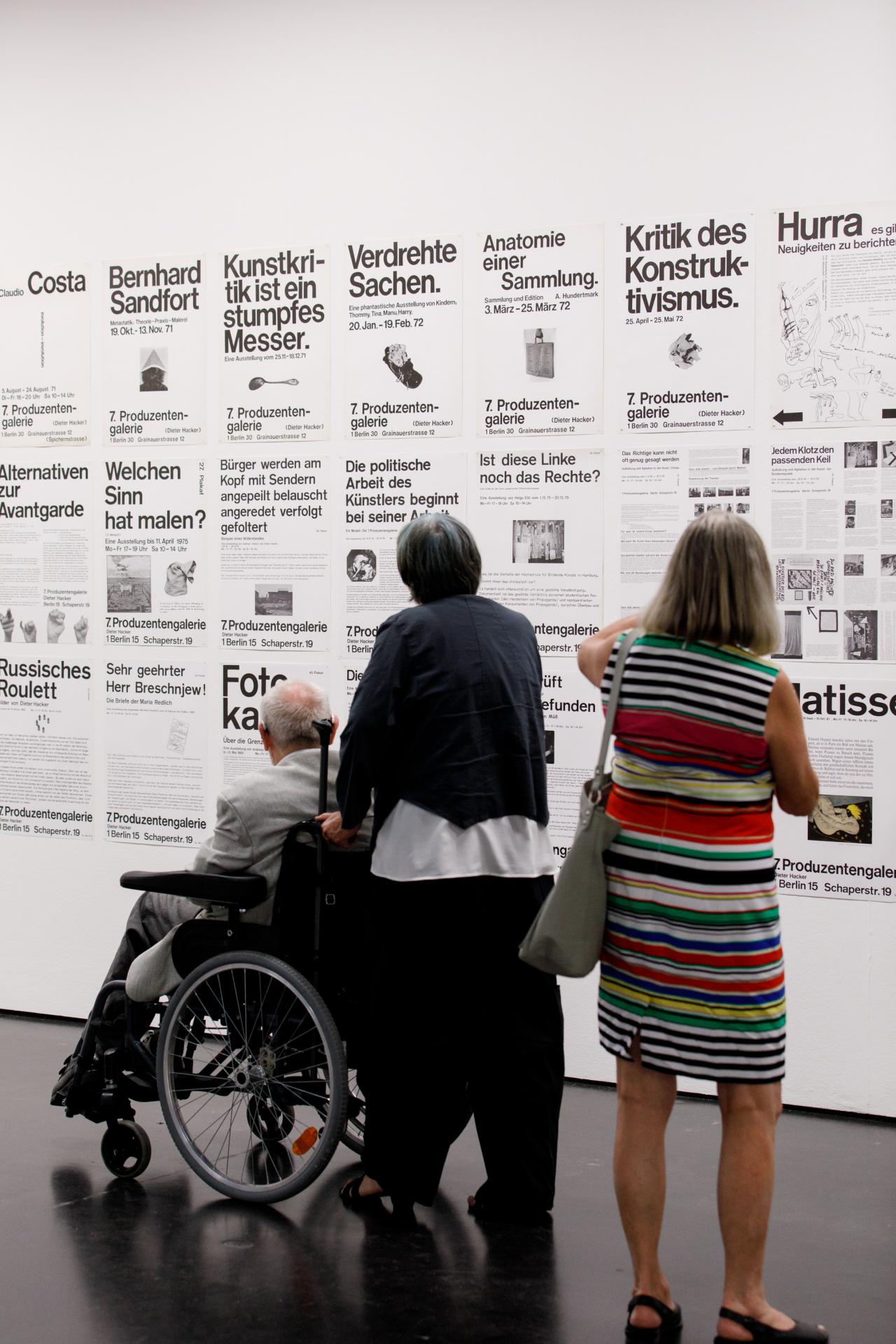 The picture shows three visitors in front of posters with typography 