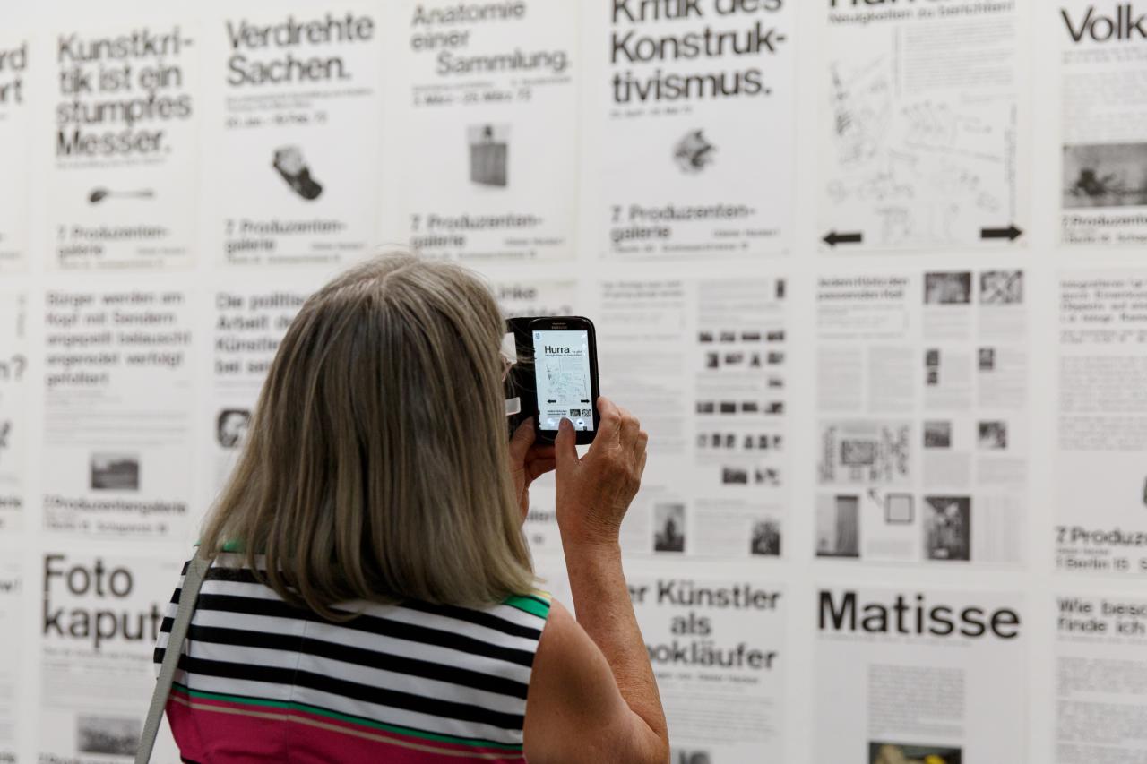 A visitor takes a picture of a wall full of typography posters with her smartphone. 