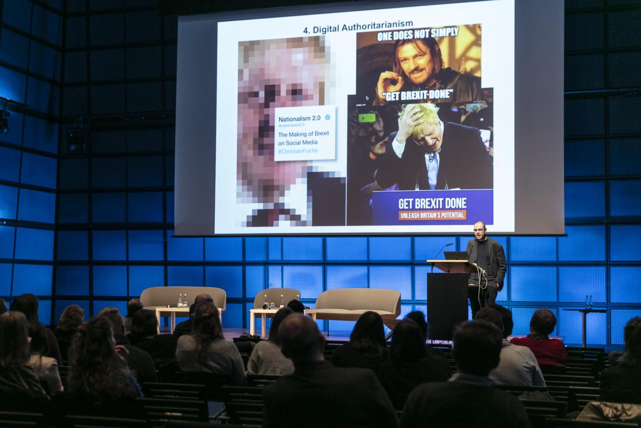Das Foto zeigt Christian Fuchs während seines Vortrages. Der letzte Vortrag der Konferenz, bei dem er mit akutellen politischen Bildern die Debatenn um Trump und Boris Johnson