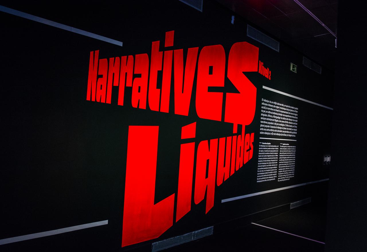 Der Schriftzug »Narratives Liquides« ist in großen roten Buchstaben in schräglage zu sehen. Rechts beginnt der Ausstellungseingang.