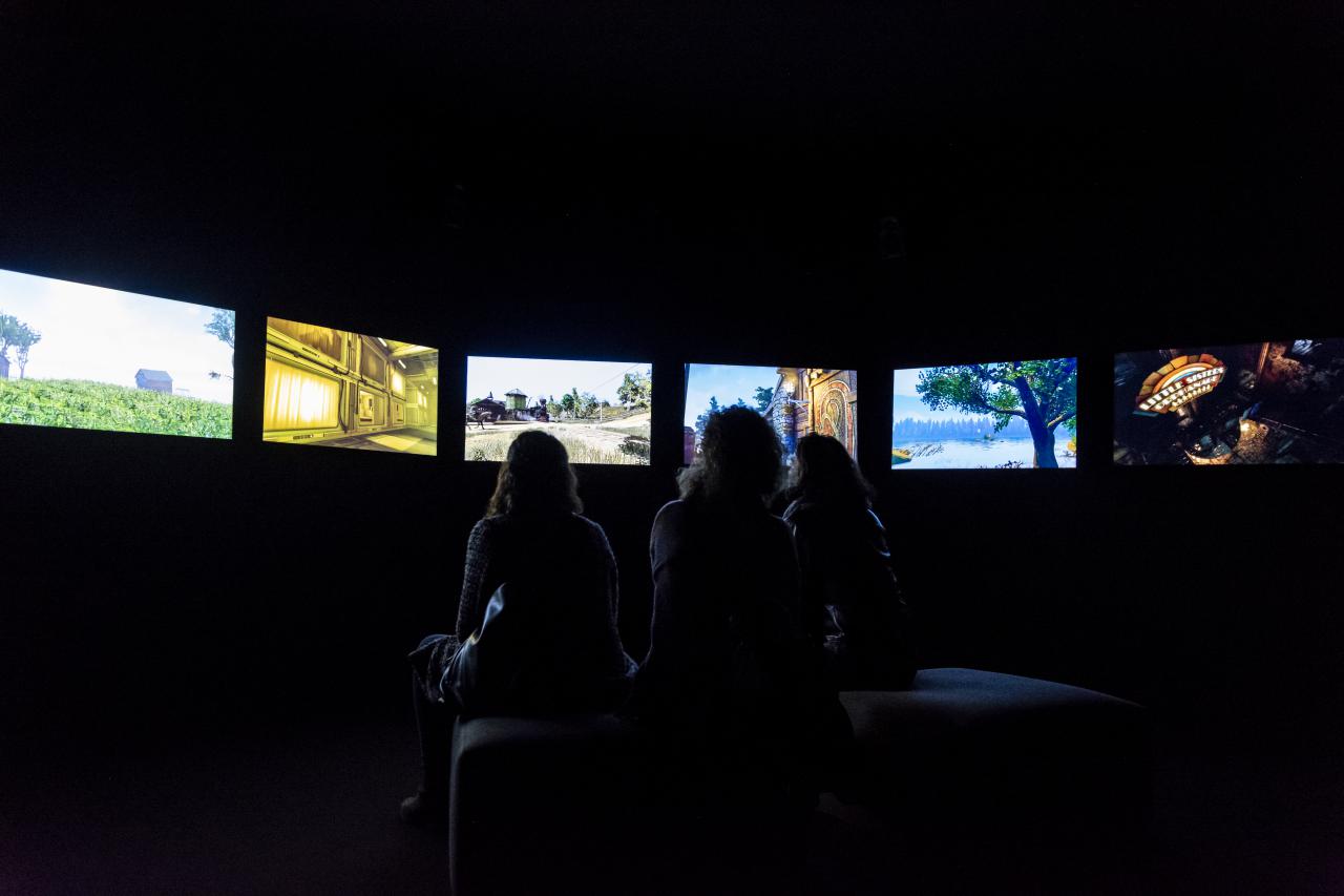Das Foto zeigt drei Frauen, die in einem dunklen Raum sitzen und deren ausschließlich ihre Silouette zu sehen ist. Im Halbkreis ist eine Bildschirmreihe zu sehen, die die Frauen umgibt.