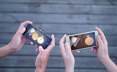 Close-up of two people holding their smartphones and playing "Tick Tock: A Tale for Two" together.