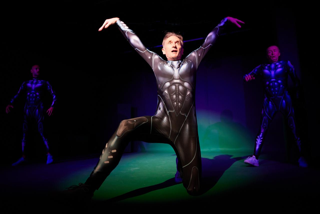 A man in futuristic armor strikes a pose in the spotlight on stage.
