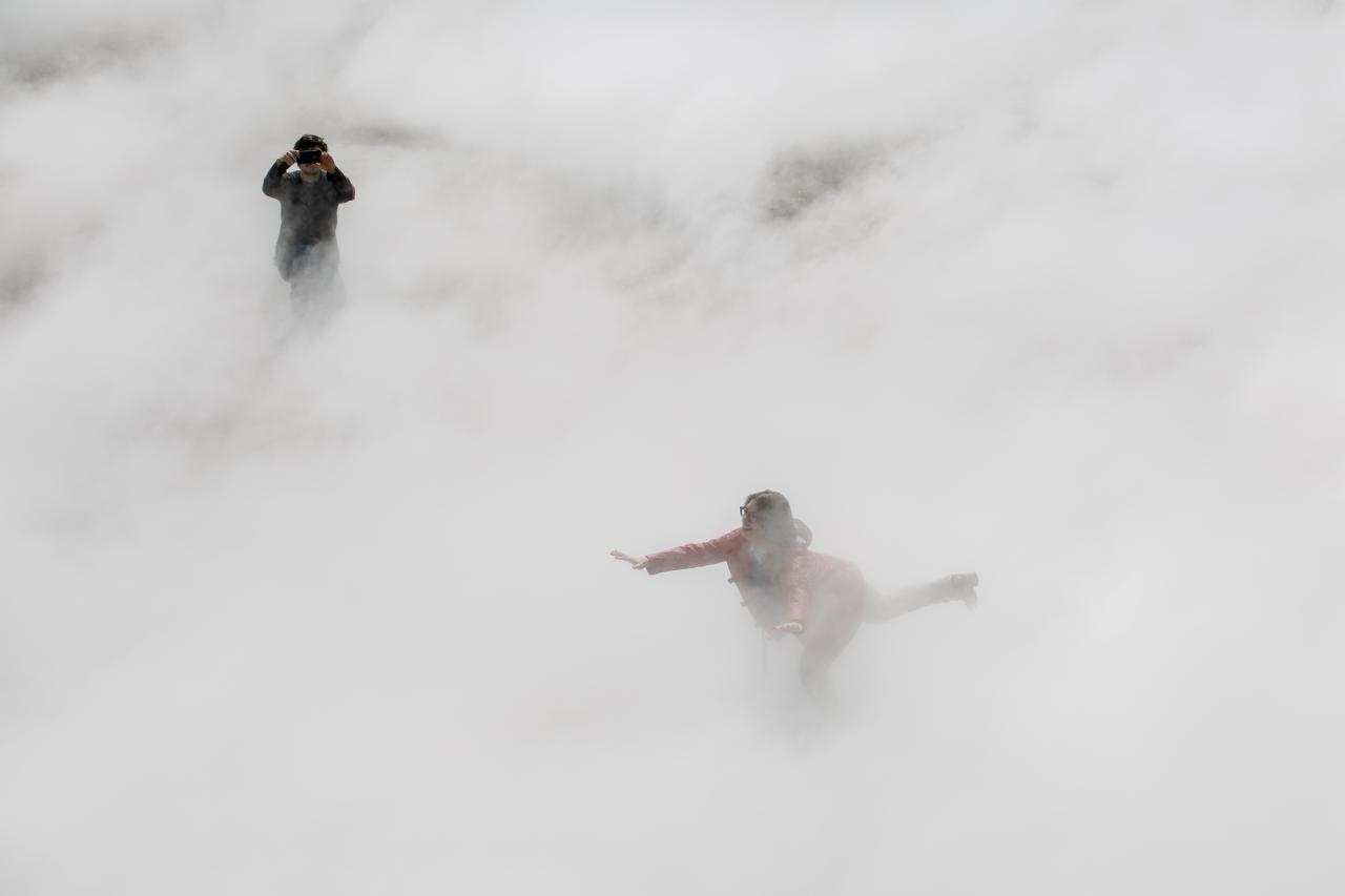 You can see a woman balancing on one leg with outstretched arms, half hidden in the fog.