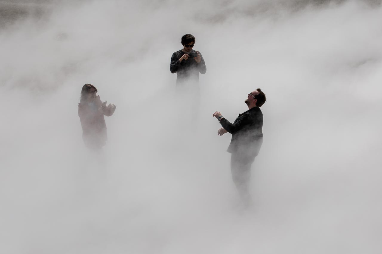 The photo shows three laughing people standing in a thick cloud of fog.