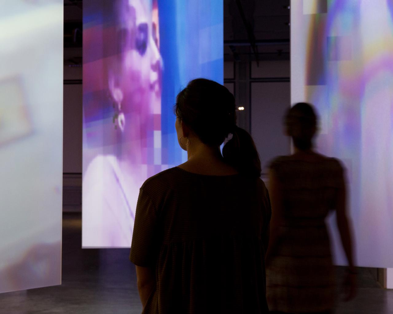The silhouettes of two visitors in front of filmed screens