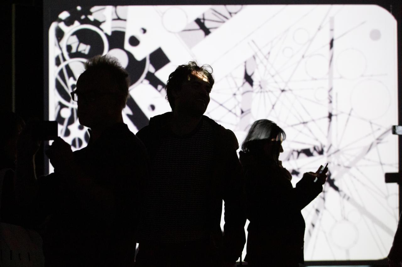 Photo of people in front of a projection screen with an abstract video in black and white - an impression of the exhibition »bauhaus.film.expanded« at the ZKM Karlsruhe.