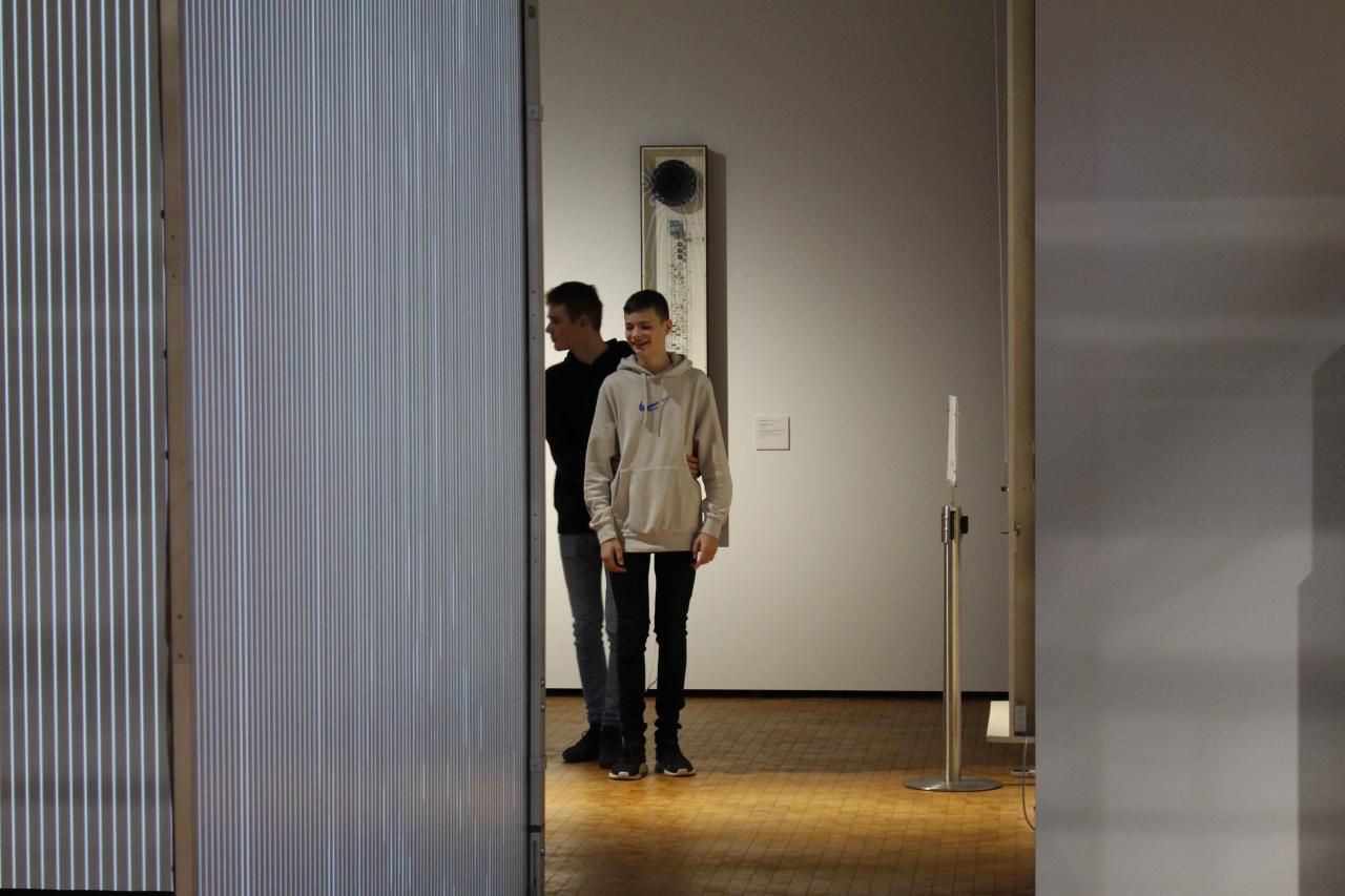 Zwei Jungs laufen mit geschlossenen Augen durch die Ausstellung »Writing the History of the Future«.