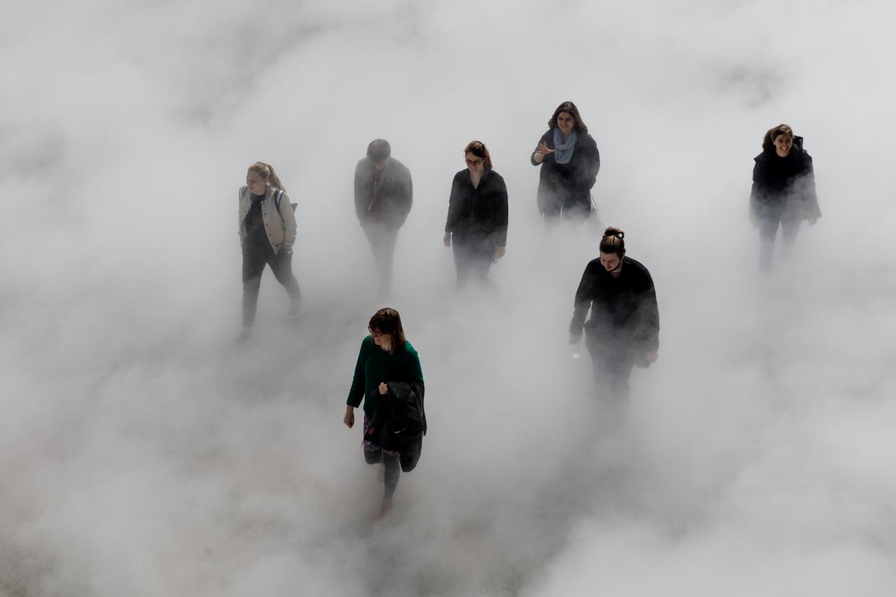 The photo shows seven laughing people walking across the Human Rights Square, partly covered by fog.