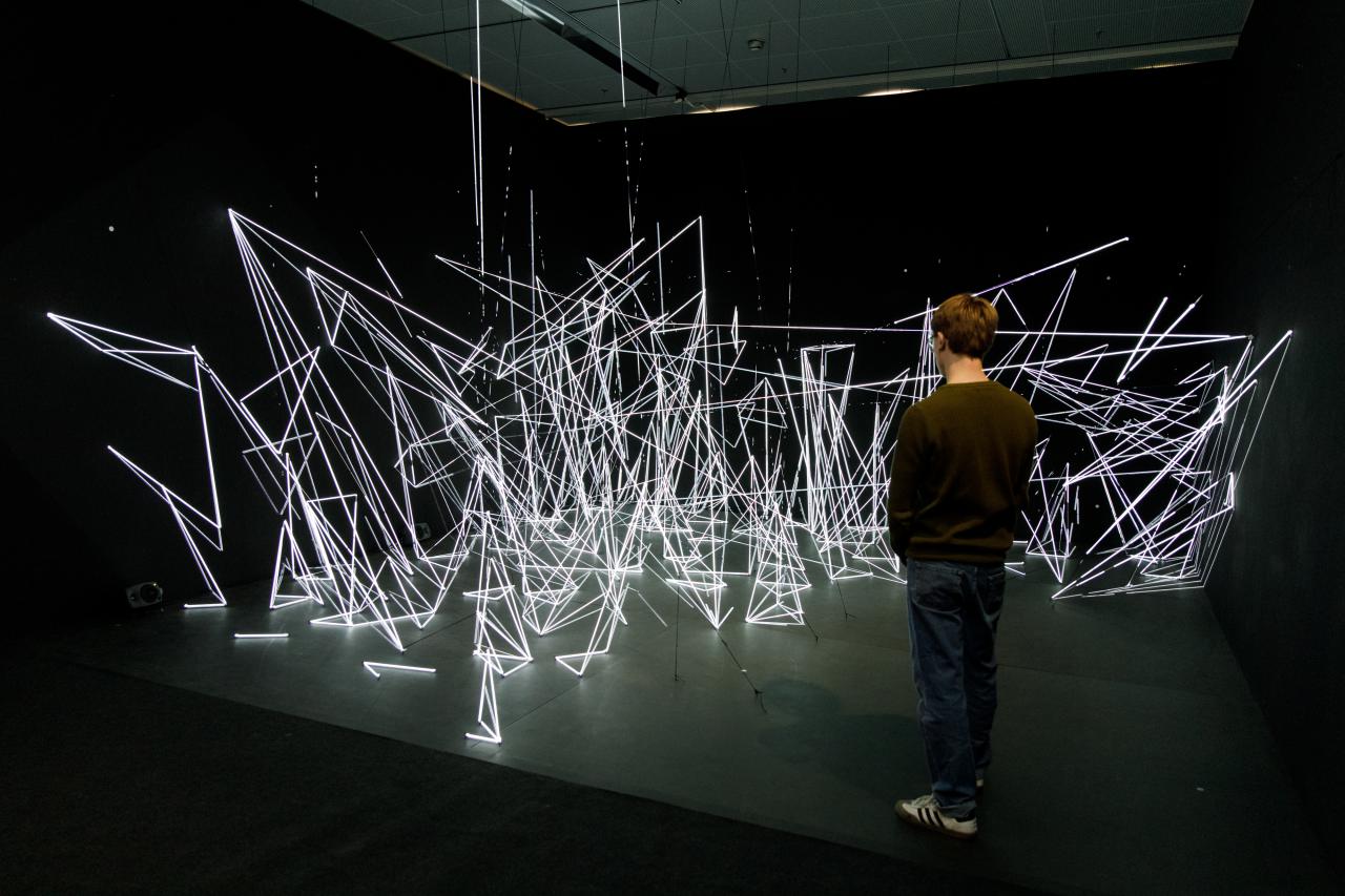 An installation of white, illuminated nylon threads in geometric shapes.