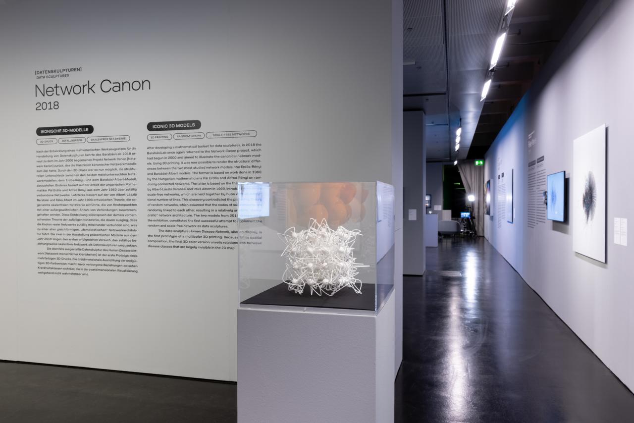 Ein Ausstellungsraum mit einem weißen 3D-Netzwerk-Modell in einem Glaskasten.