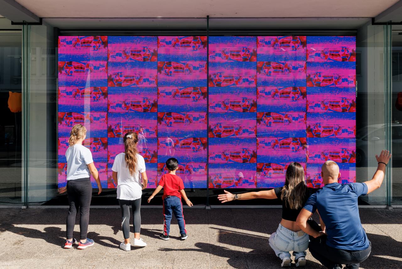 In the picture you can see the video installation "footprint" by Jonas Denzel. On a large screen there are many small pictures taken from the legs of passers-by. A family of five stands in front of it and interacts with the artwork.