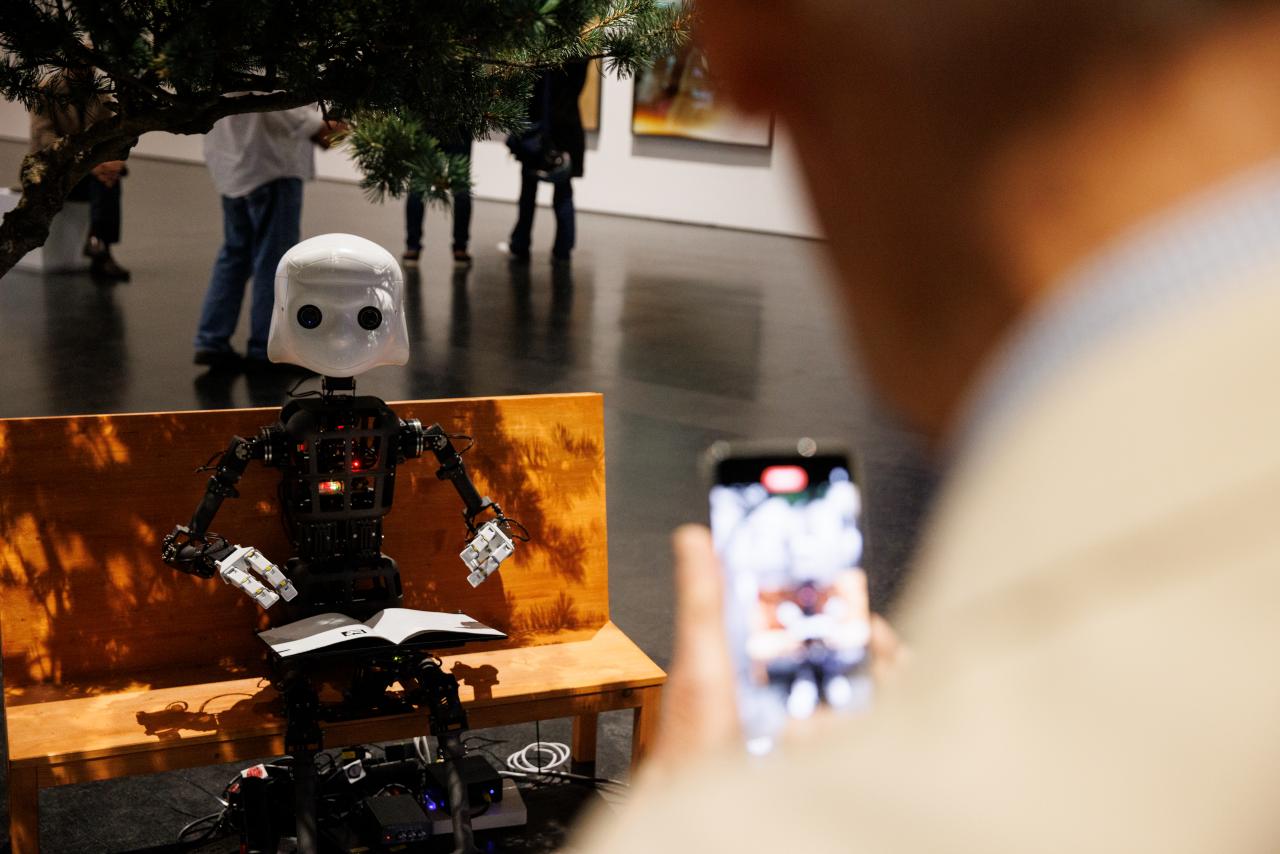 On display is a robot whose structure resembles the body of a human being. He is sitting on a bench.