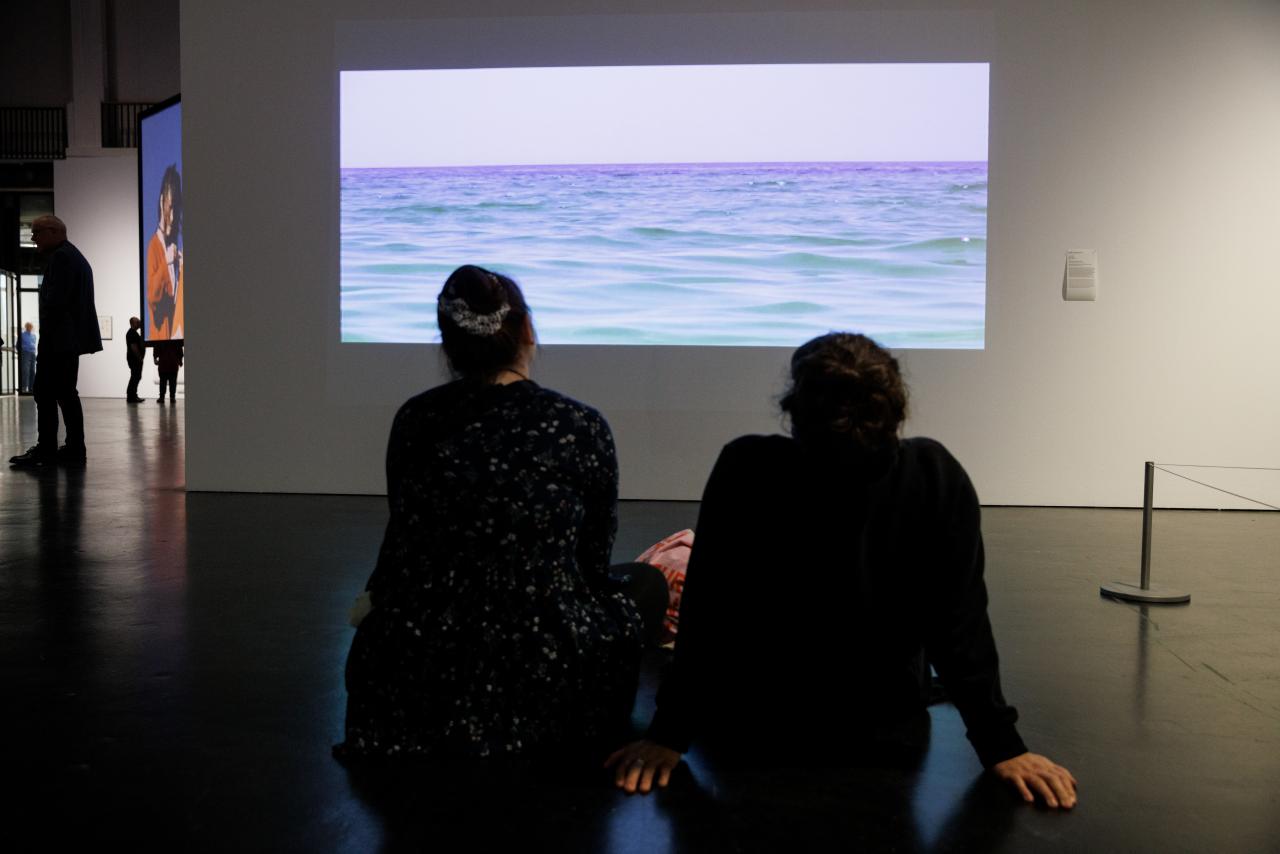 You can see two people sitting in front of a screen. On the picture you can see the sea.