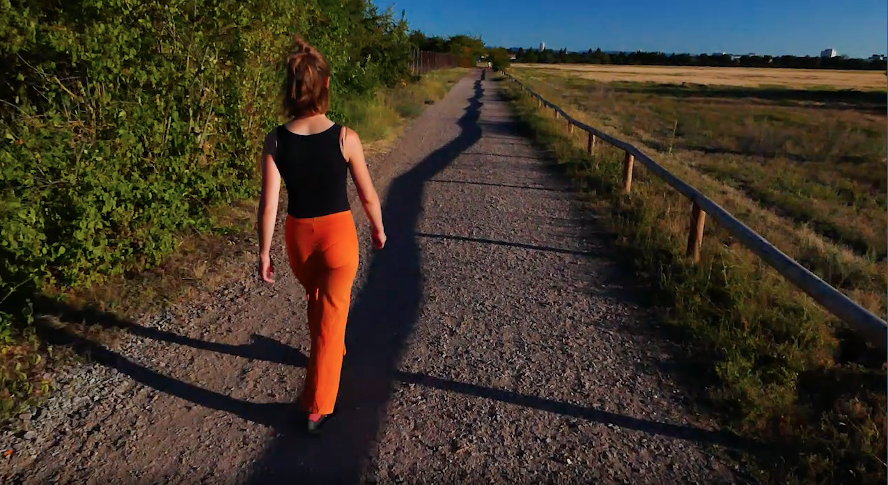 The image shows a person walking along a shadow in the nature.