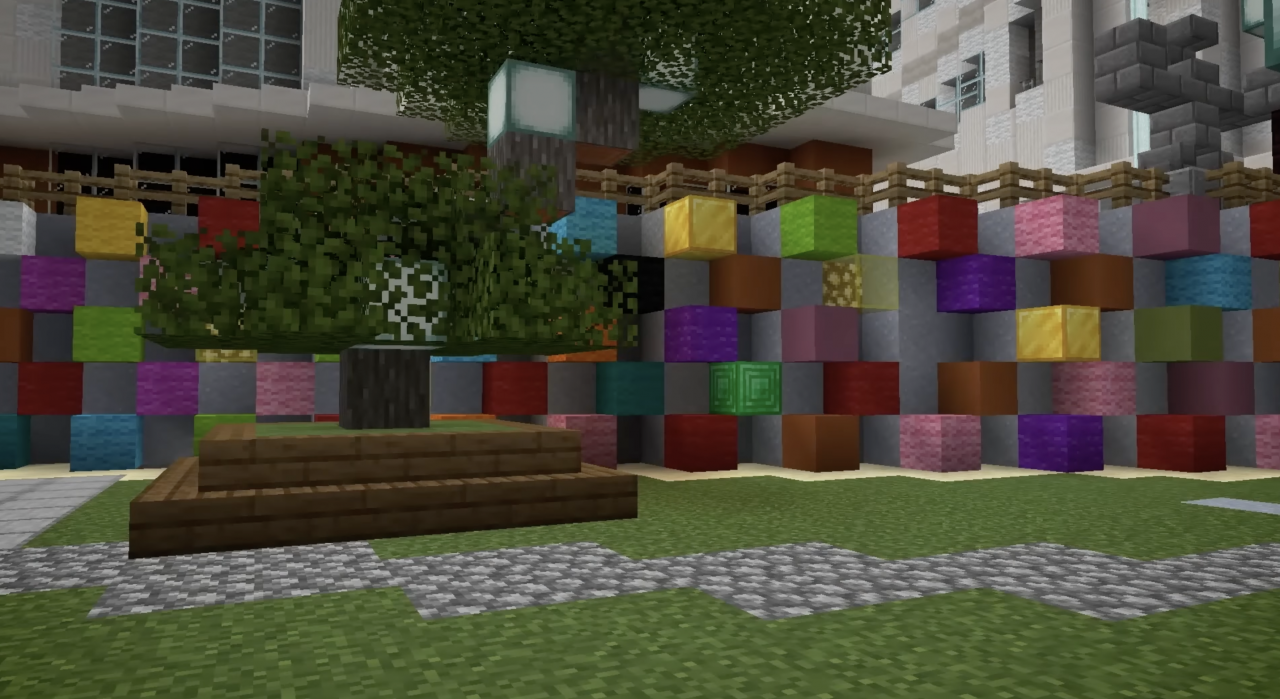 Minecraft view of a representation of the urban space. A tree is shown in the centre of the image. Behind it is a wall in grey and coloured blocks.