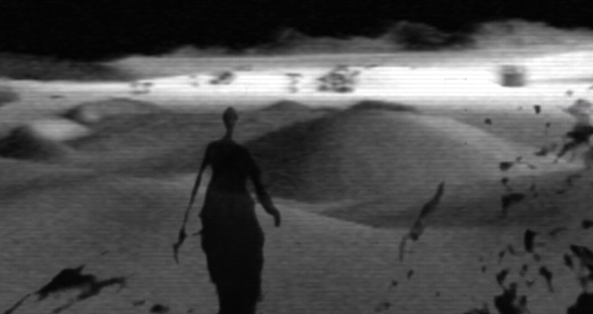 Das Bild ist in schwarz-weiß, eine schattenhafte Gestalt wandert durch die Wüste