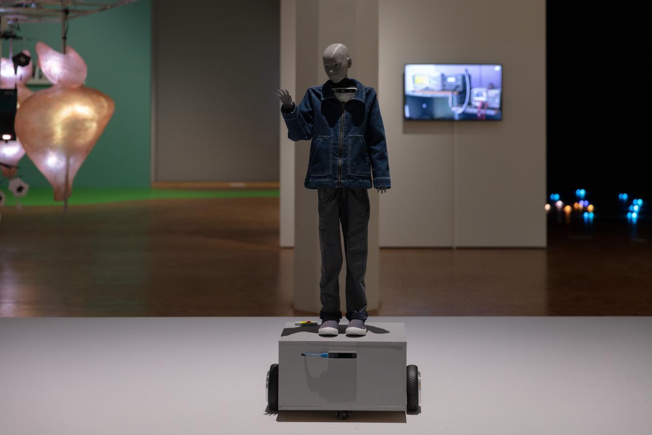 Anna Dumitriu & Alex May, »Cyberspecies Proximity«, 2020. In the picture there is a human-like robot raising his hand. He is wearing jeans clothes.