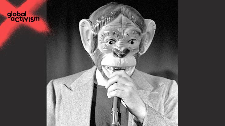Ein Mann mit einer Affenmaske spricht in eine Mikrofon