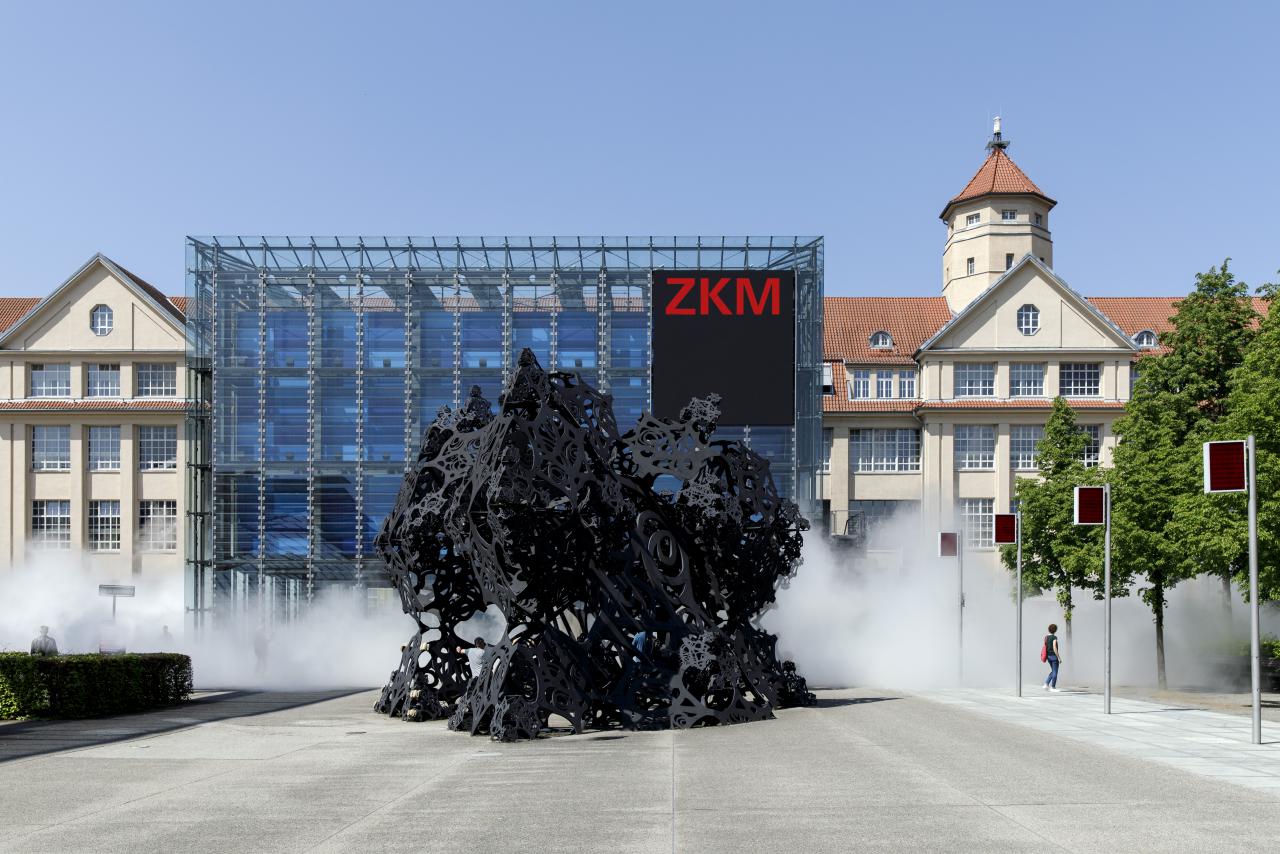 The photo shows the entrance of the ZKM as well as the cube surrounded by a light fog.