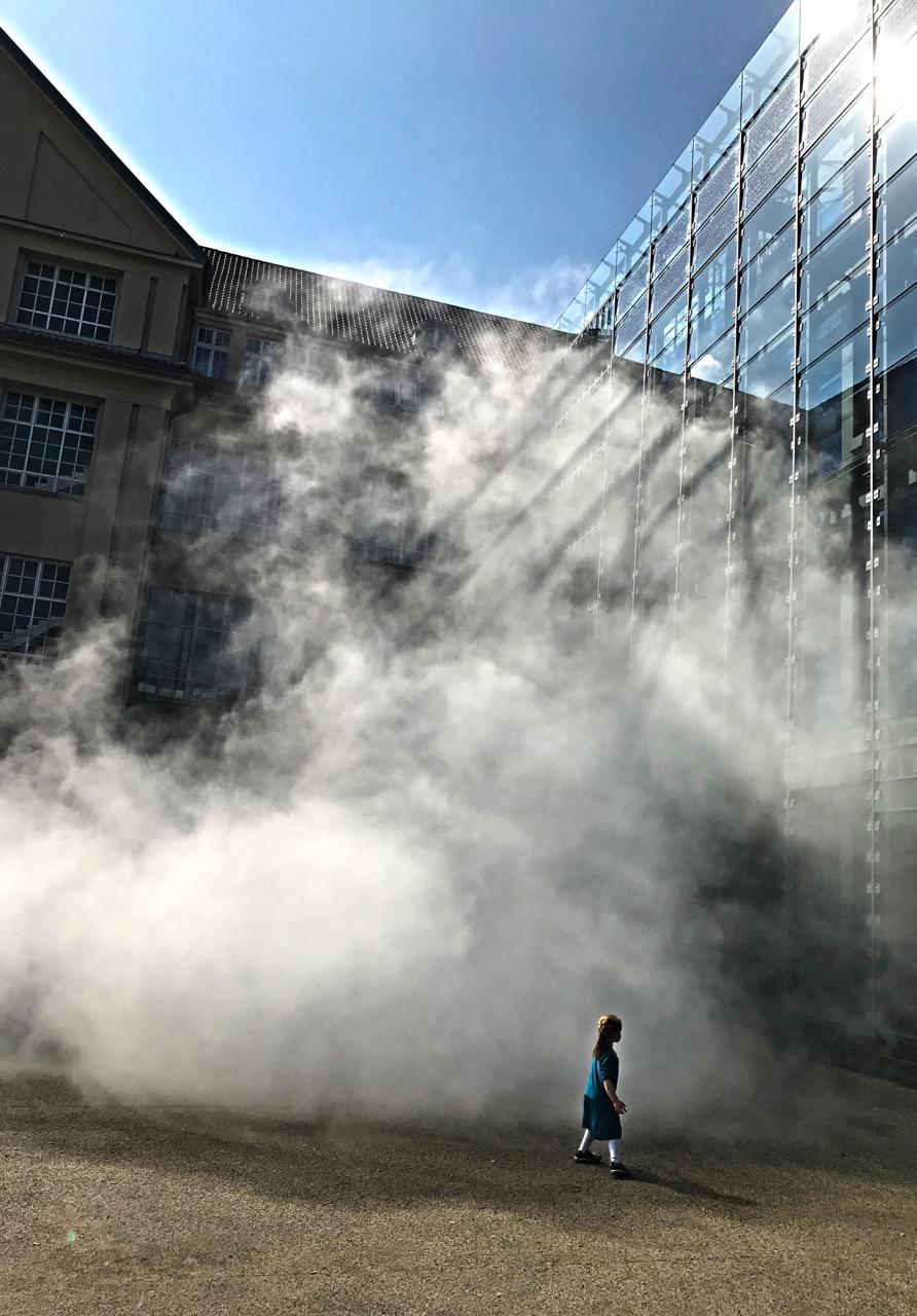 A sculpture of fog encloses a glass building.