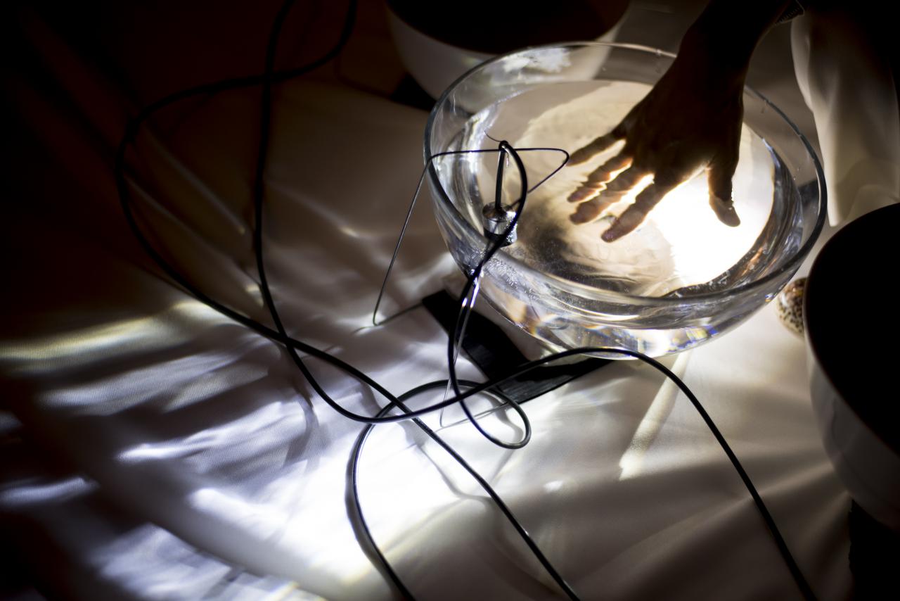 Photo of a hand in a glass bowl filled with water. A microphone is hanging in the bowl.