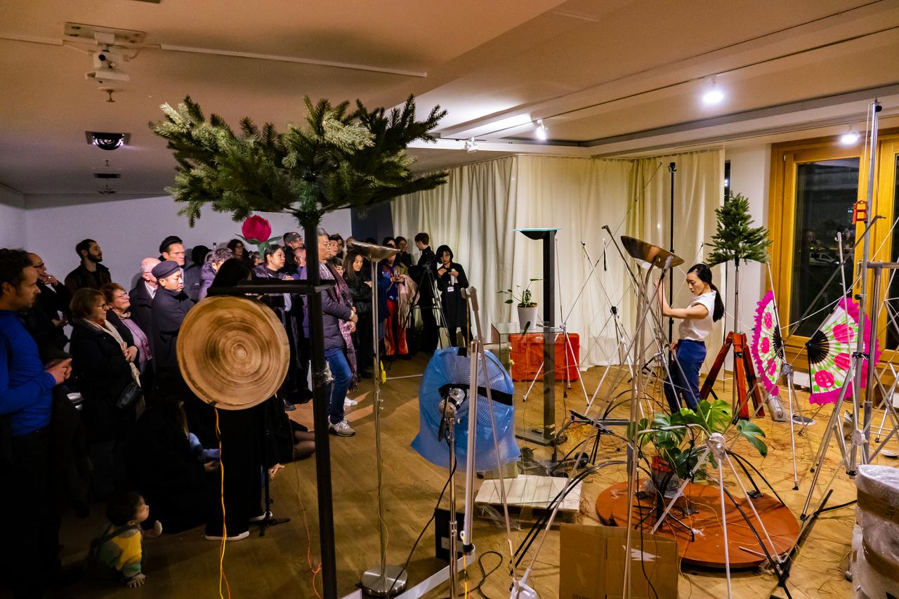 The cultural space Korea can be seen in Berlin during a performance. On the left side the visitors are standing while on the right side a performer moves between different sound objects.