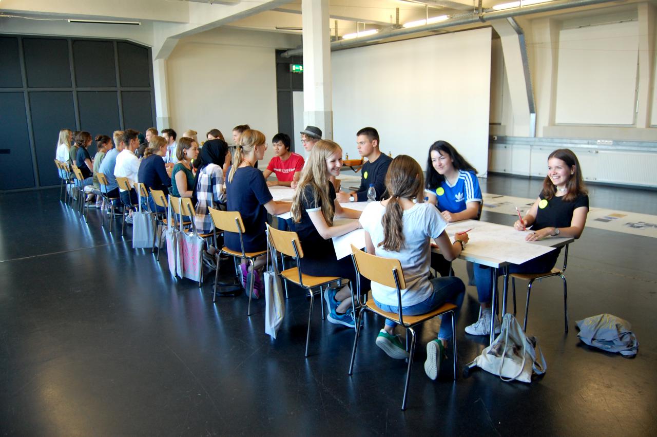 Many young pupils sit at a table within the framework of an event of the cultural academy.