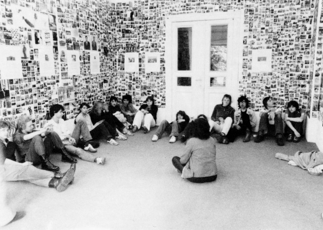 Young people sit in a room whose walls are covered with photographs.