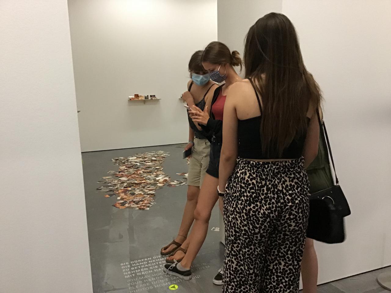 You can see three girls who have put their feet on a text on the floor and take a photo of it.