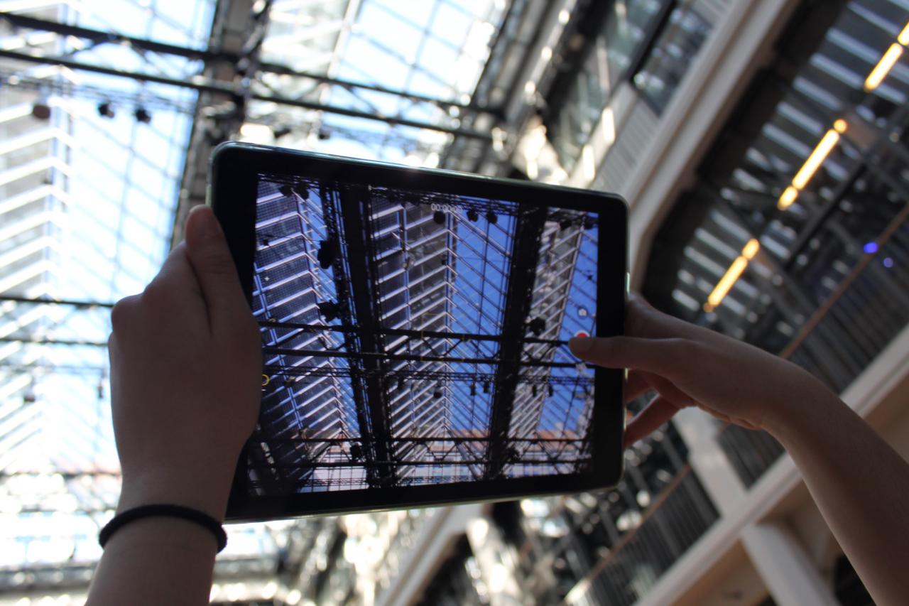 Two hands taking a photo of the ceiling of the ZKM with an iPad during the event »Global Sound«. 