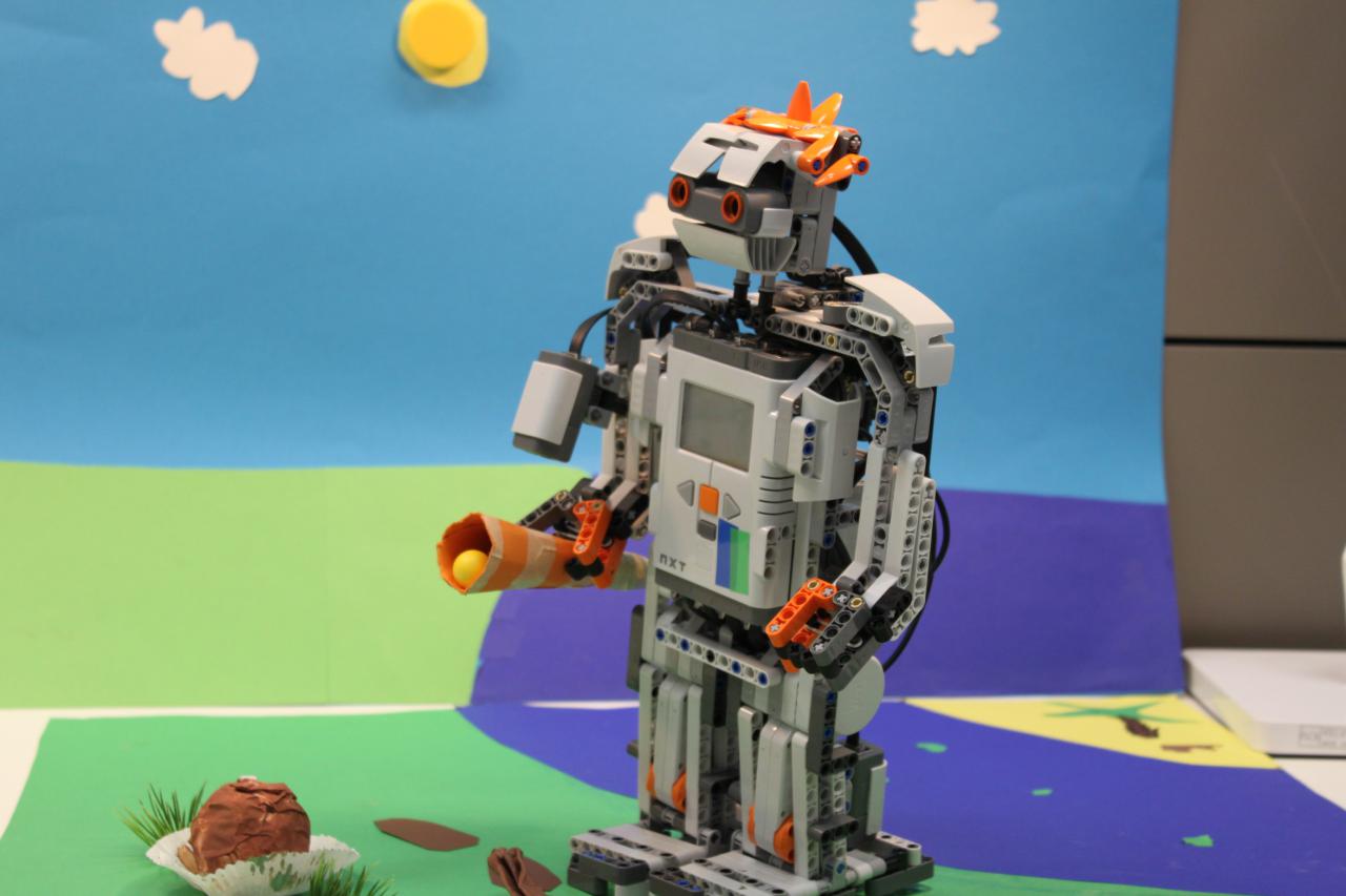 In front of a paper-set on which a sun and clouds are glued on, we can see a lego-robot.