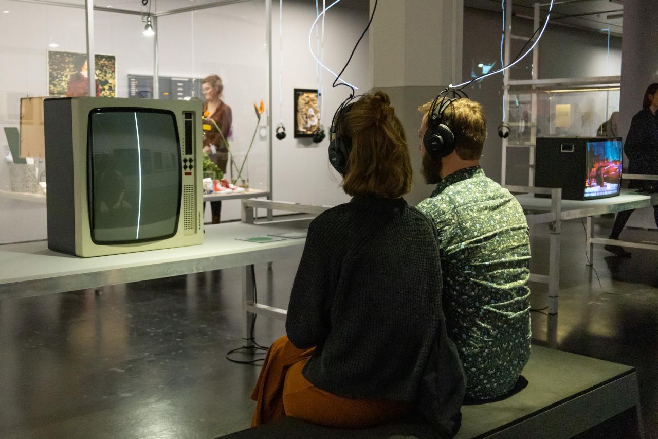 Ausstellungsansicht »Matter. Non-Matter. Anti-Matter« im ZKM | Zentrum für Kunst und Medien Karlsruhe, 2022. Zu sehen sind zwei sitzende Personen mit dem Rücken zur Kamera. Sie tragen Kopfhörer.