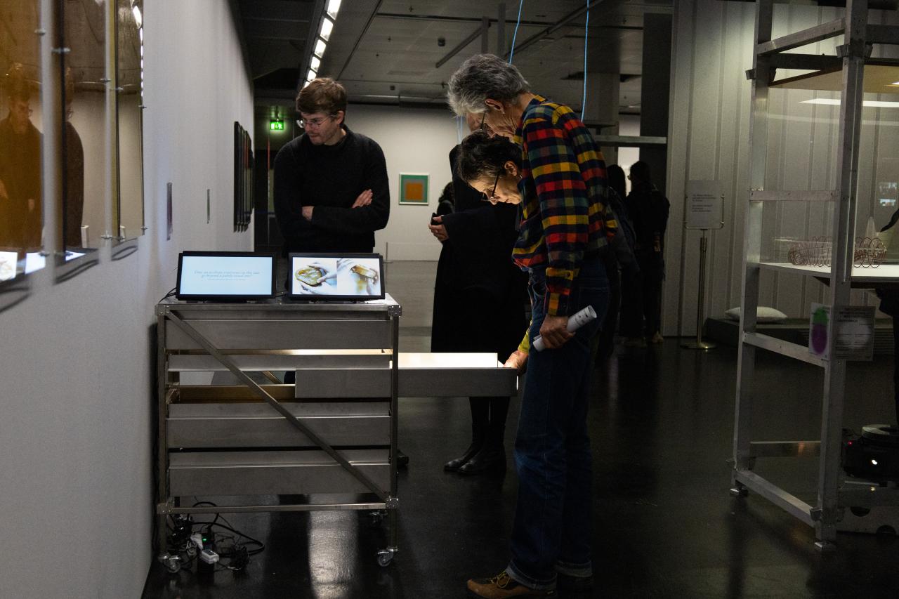 Exhibition view »Matter. Non-Matter. Anti-Matter« at ZKM | Center for Art and Media Karlsruhe, 2022. People are seen around a cart on which tablets are. Two people have opened a drawer and are looking at its contents.