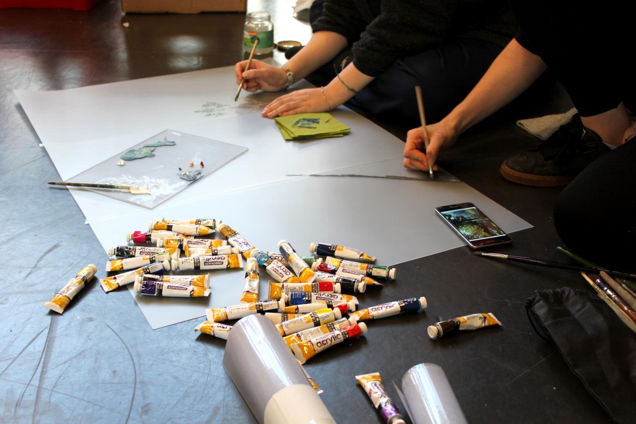 Many painting hands on paper and different paint tubes can be seen at an event of the cultural academy.