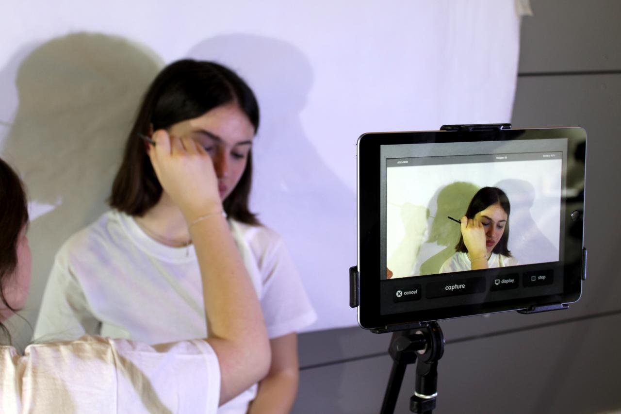Zu sehen ist ein Mädchen, das vor einer Kamera geschminkt wird im Rahmen einer Veranstaltung der Kulturakademie.