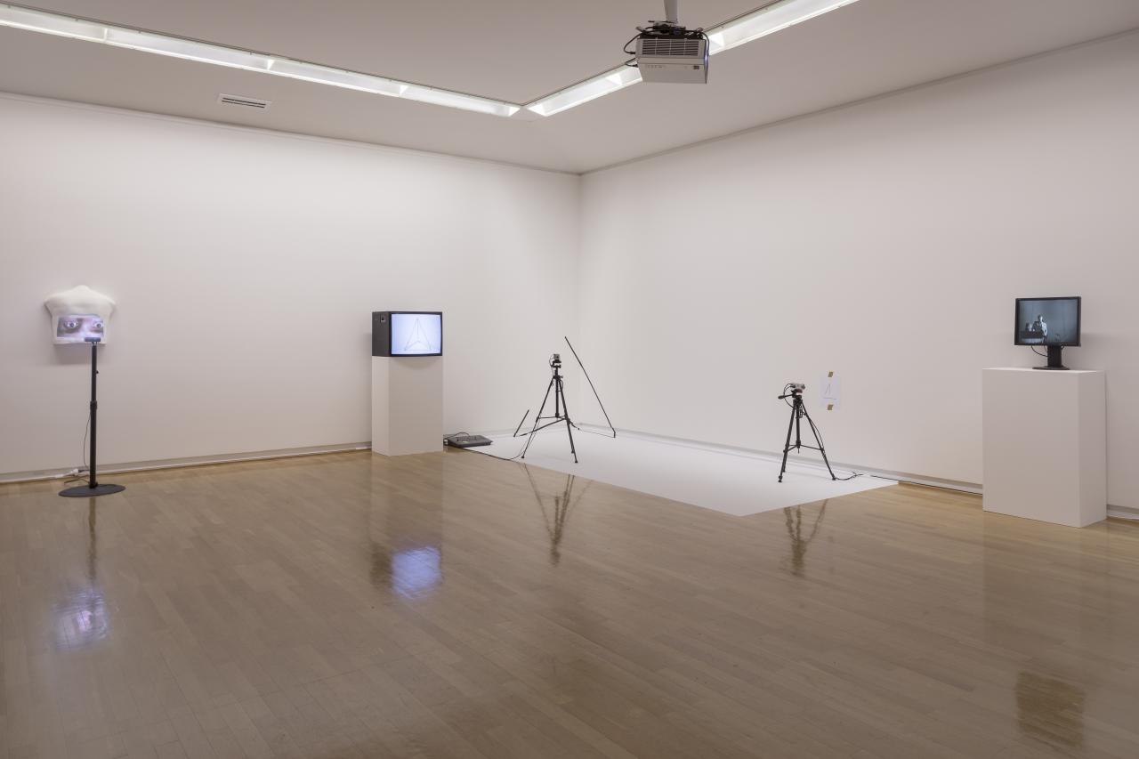 You can see the corner of a room with four objects. You can see two screens and two tripods, which are placed in a large distance to each other. 
