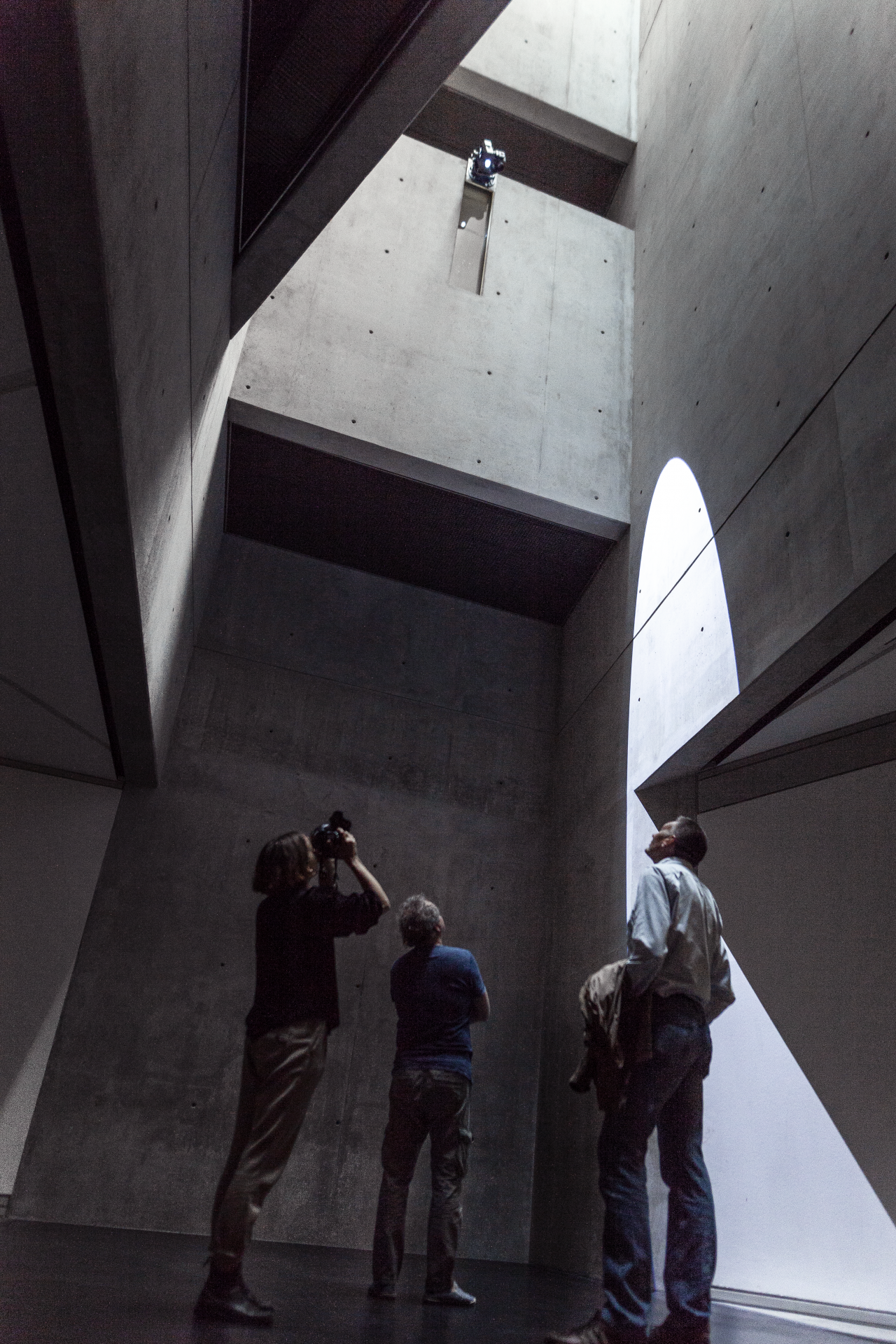 You can see 3 people in a high room with concrete walls where the sunlight shines in from above