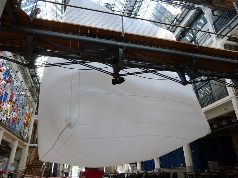 A very large white Baloon is hanging in an atrium