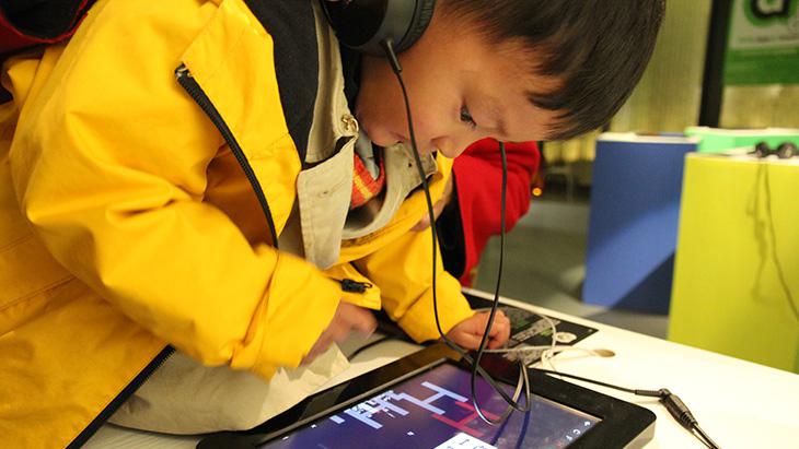 Ein Junge mit Kopfhörern beugt sich über ein Tablet-Computer