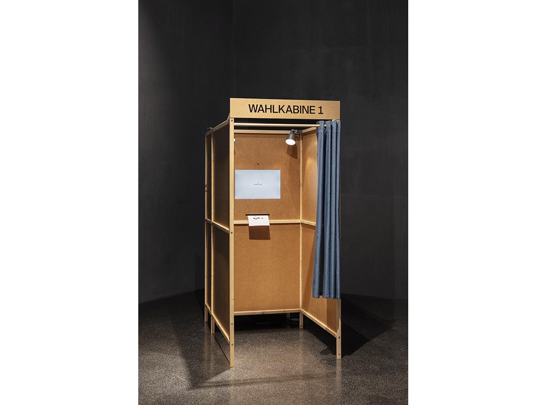 Wahlkabine aus Holz, darin ein Bildschirm