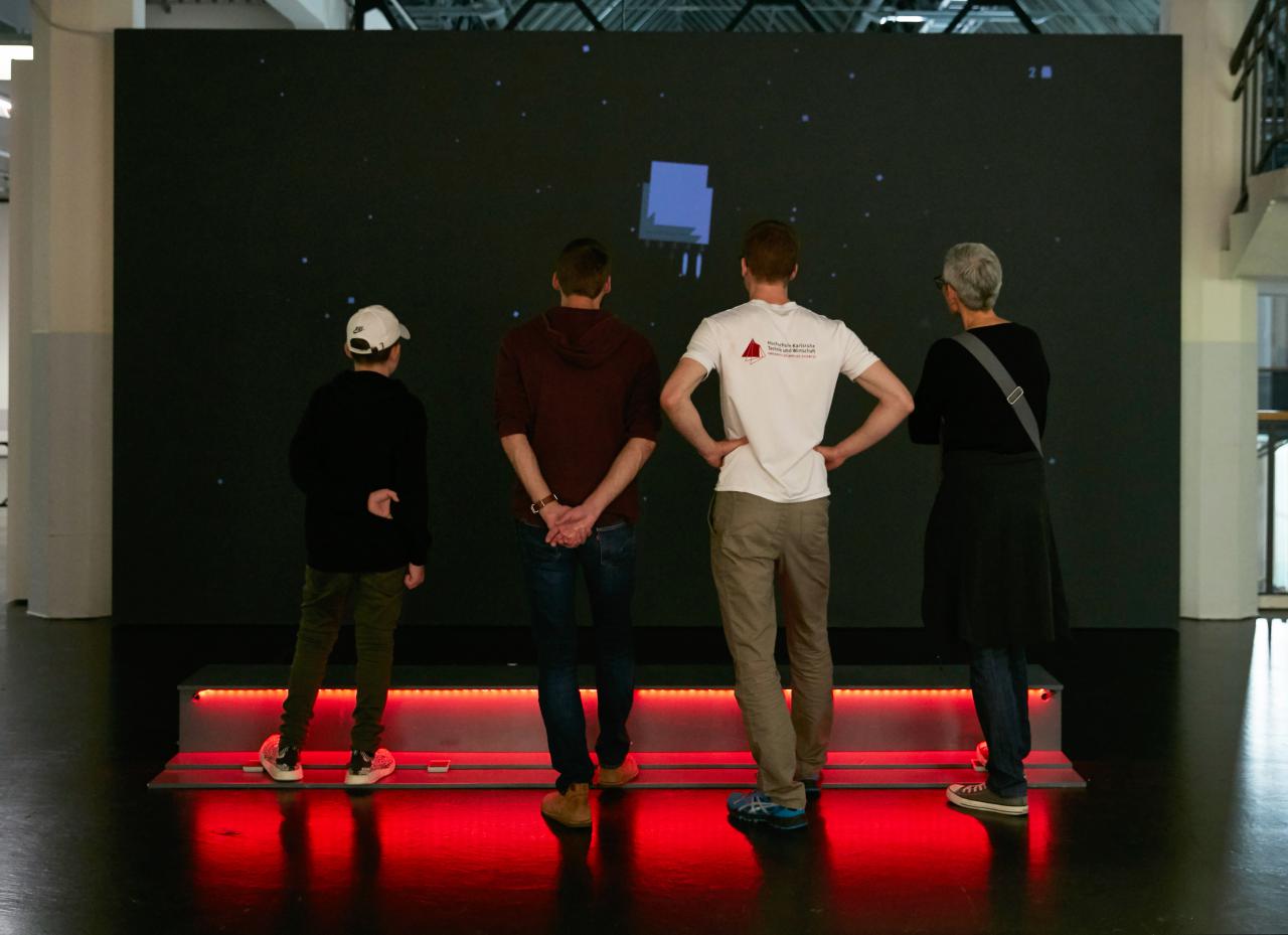 Vier Personen stehen vor der Installation des Computerspiels »Rakete«.