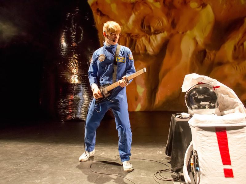 You can see a young man in a blue astronaut suit and a guitar in his hand.