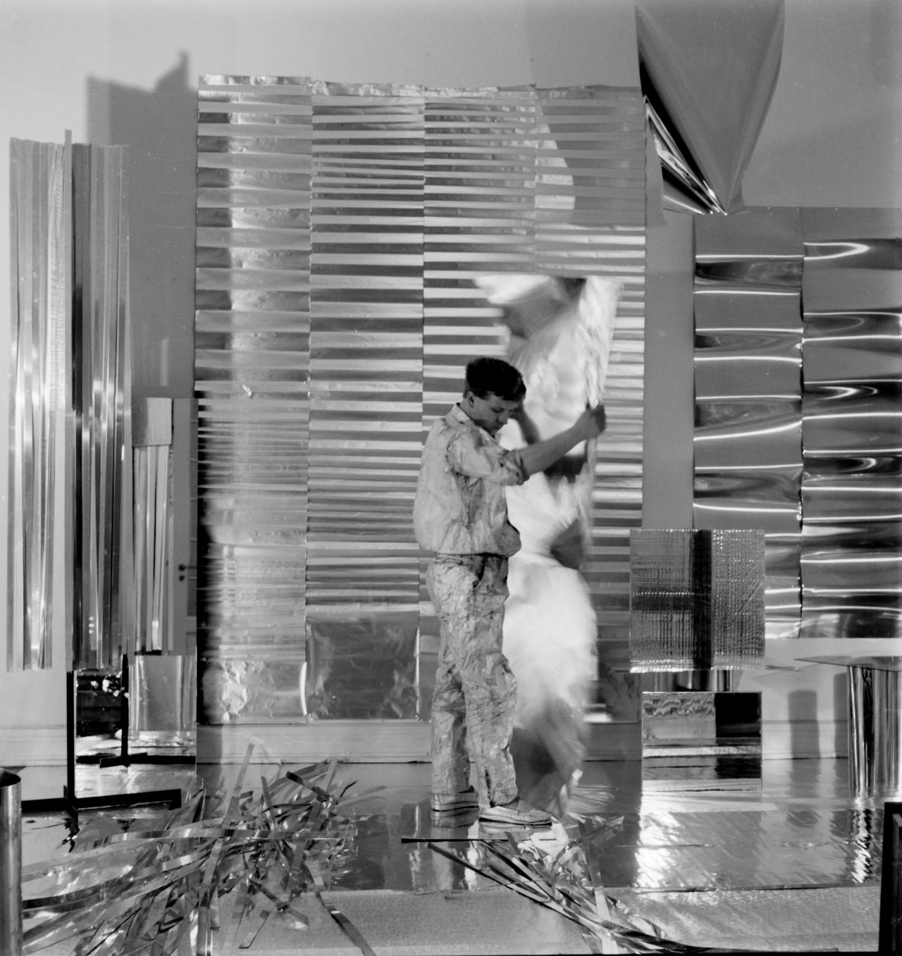 Heinz Mack steht in seinem Atelier in Düsseldorf. Das Bild wurde im Jahr 1959 aufgenommen und um ihn herum befinden sich seine Skulpturen und Werke. Das Bild ist schwarz-weiß.