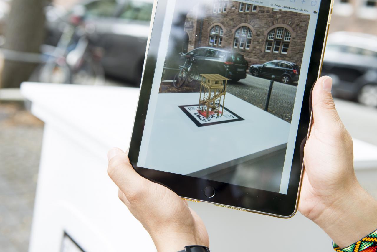 Auf einem Tablet-Bildschirm ist eine virtuelle Skulptur zu sehen, den realen Raum eingebettet ist.