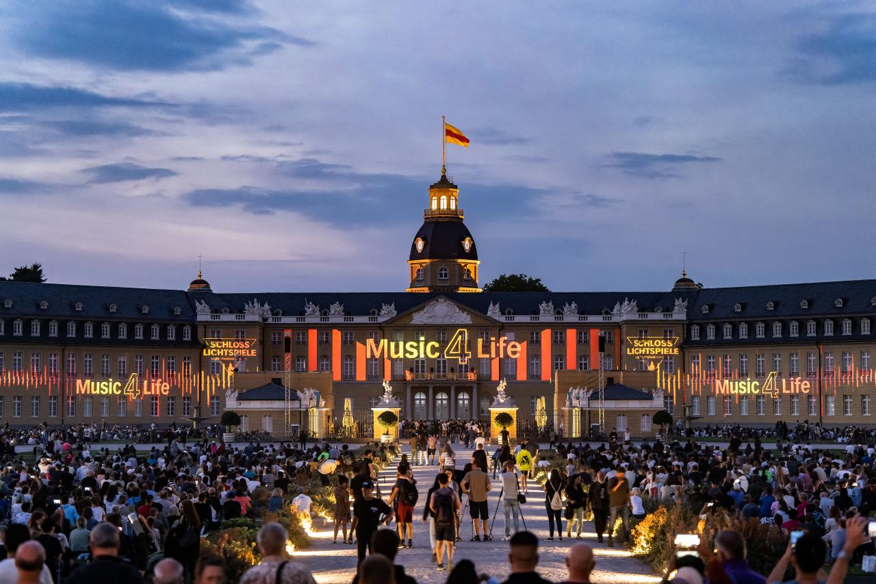 Zu sehen ist die Eröffnung der Schlosslichtspiele. Das Schloss Karlsruhe leuctet unter dem Motto Musik 4 Life, welches an die Fassade projeziert ist.