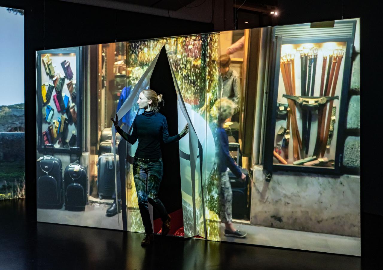 Ausstellungsansicht »Marijke van Warmerdam. Then, now, and then«. Zu sehen ist eine Person, die durch einen Vorhang tritt, auf dem ein Video projiziert wird.