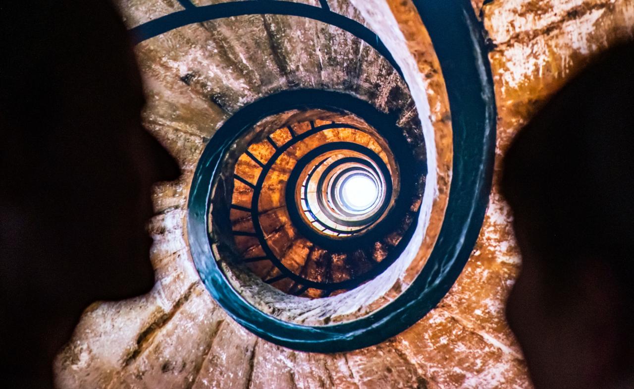 You can see a shot of a spiral staircase. On the left and right are the shadows of two heads.