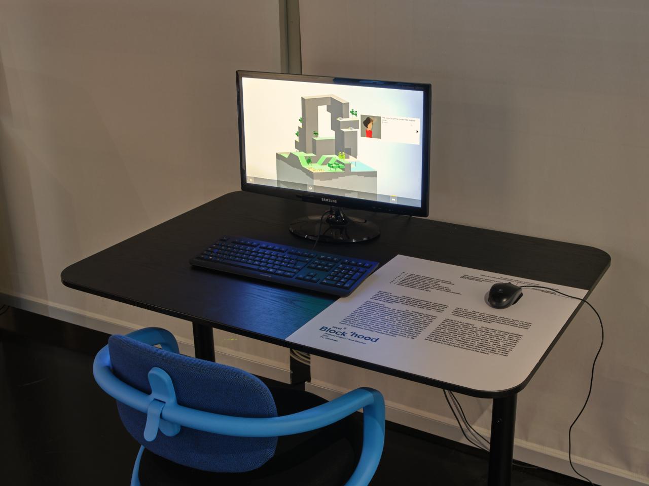 Ein blauer Stuhl steht vor einem Schreibtisch. Auf diesem Tisch steht ein Computerbildschirm mit angeschlossener Tastatur und Maus. Das Computerspiel »Block’hood« wird auf dem Bildschirm ausgespielt.